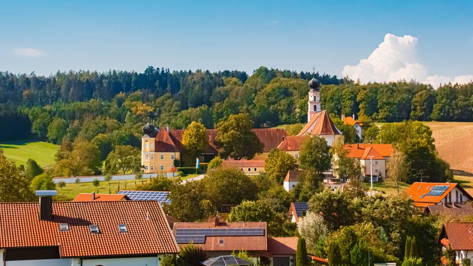 A village with traditional architecture, a church with a bell tower, and solar panels on rooftops.
