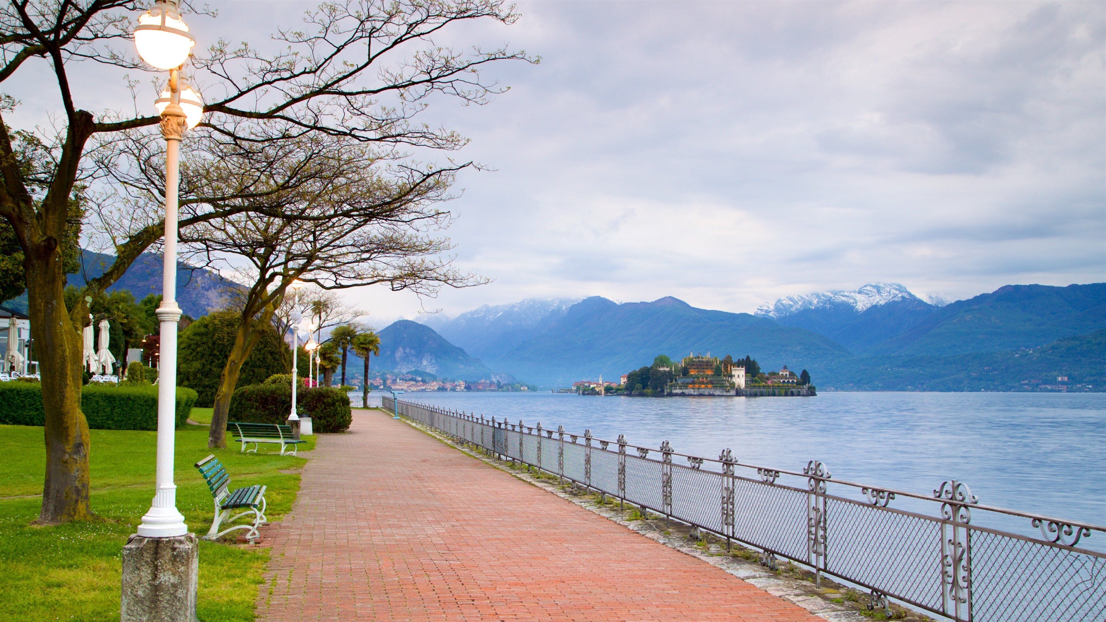 A lakeside walkway with benches, a lamp post, and a fence.