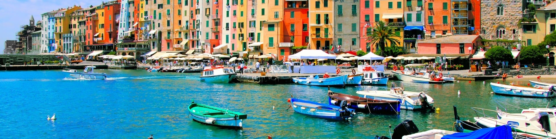 Un muelle colorido con barcos amarrados, un edificio histórico con una torre y un castillo en una colina.