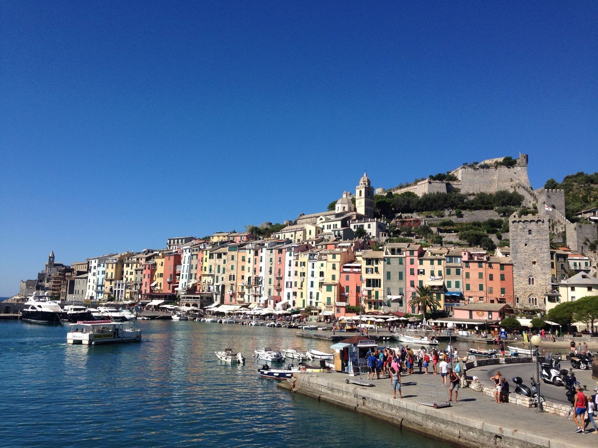 Una cittadina costiera con edifici colorati, un'antica fortezza e barche ormeggiate lungo il lungomare.