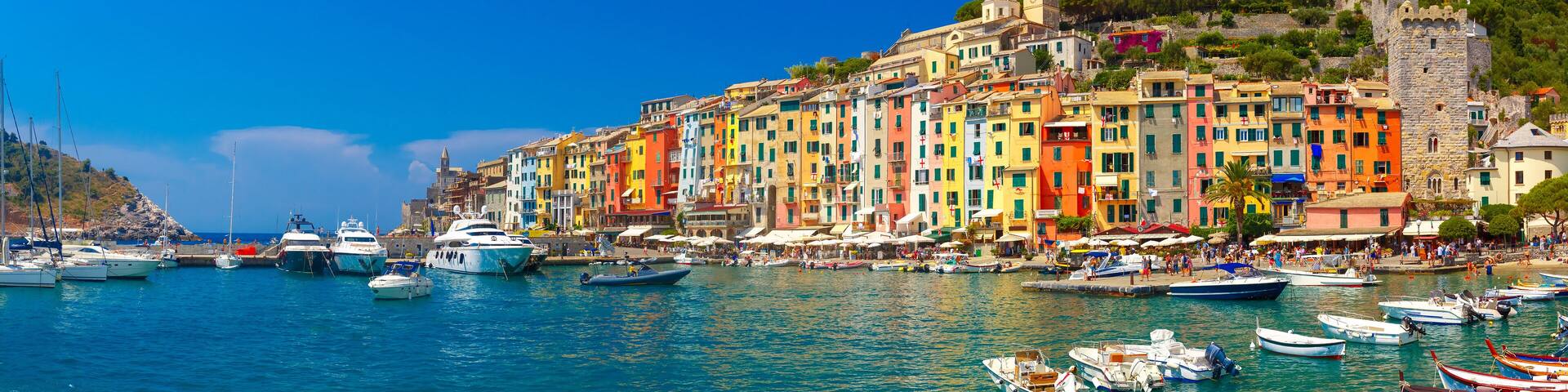A coastal town with colorful buildings, a castle, and numerous boats docked along the waterfront.