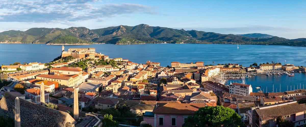 A coastal town with historic buildings, a fortified structure, and a marina.