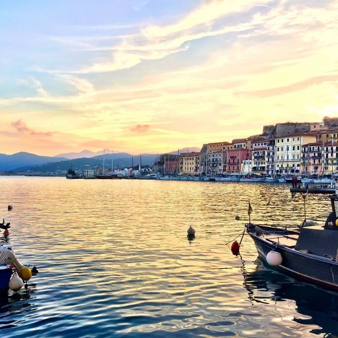A waterfront with boats, a calm sea, and colorful buildings along the shore.