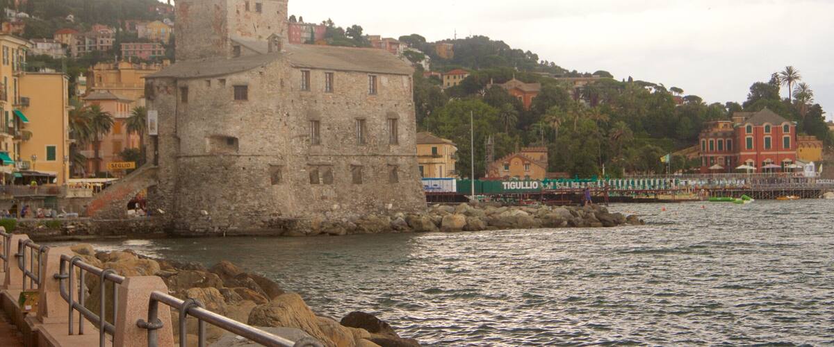 A coastal town with a prominent stone tower, colorful buildings, and a pier extending into the water.