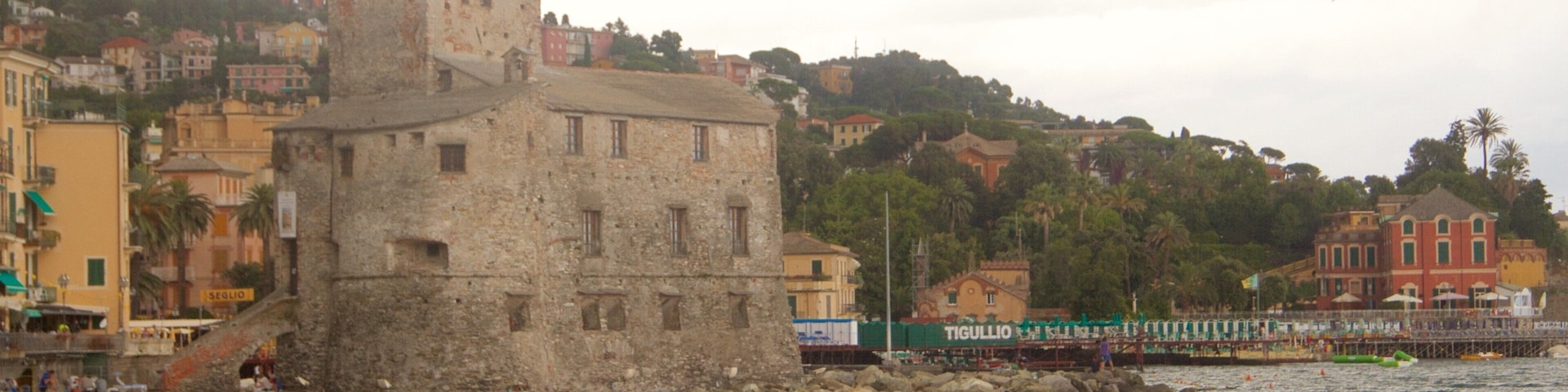 A coastal town with a prominent stone tower, colorful buildings, and a pier extending into the water.