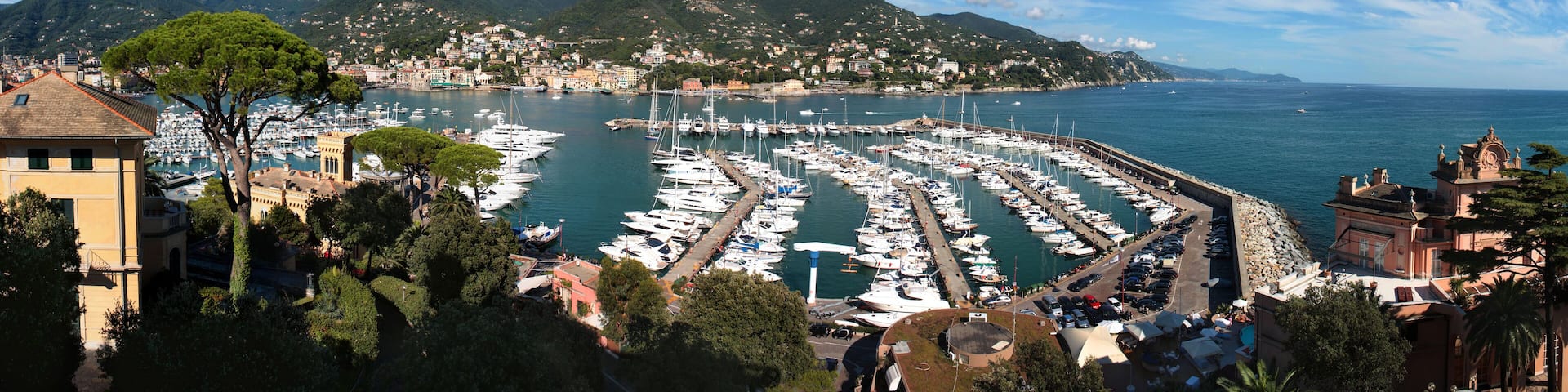A marina with numerous boats docked, surrounded by lush green hills and a clear blue sky.