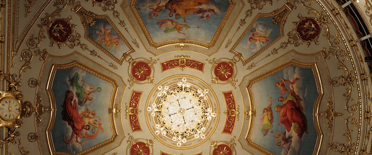 A ceiling with ornate gold and red decorations, including a central clock and surrounding frescoes.