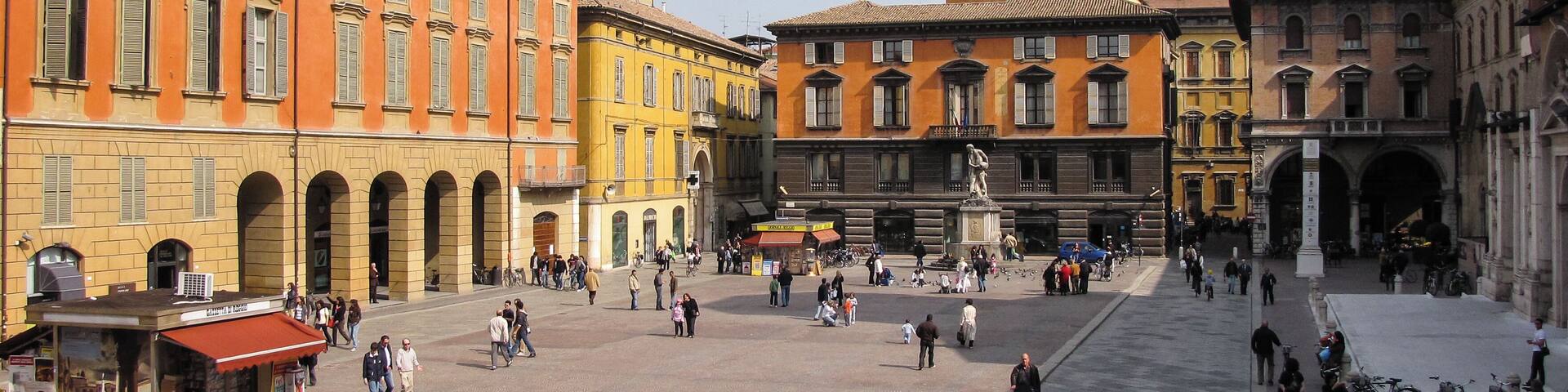 A historic square with a prominent clock tower, colorful buildings, and a central open space.