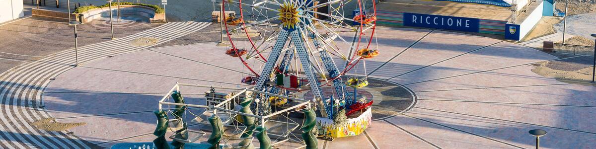 Une grande roue, une plage et un bâtiment portant l’inscription « RICCIONE ».