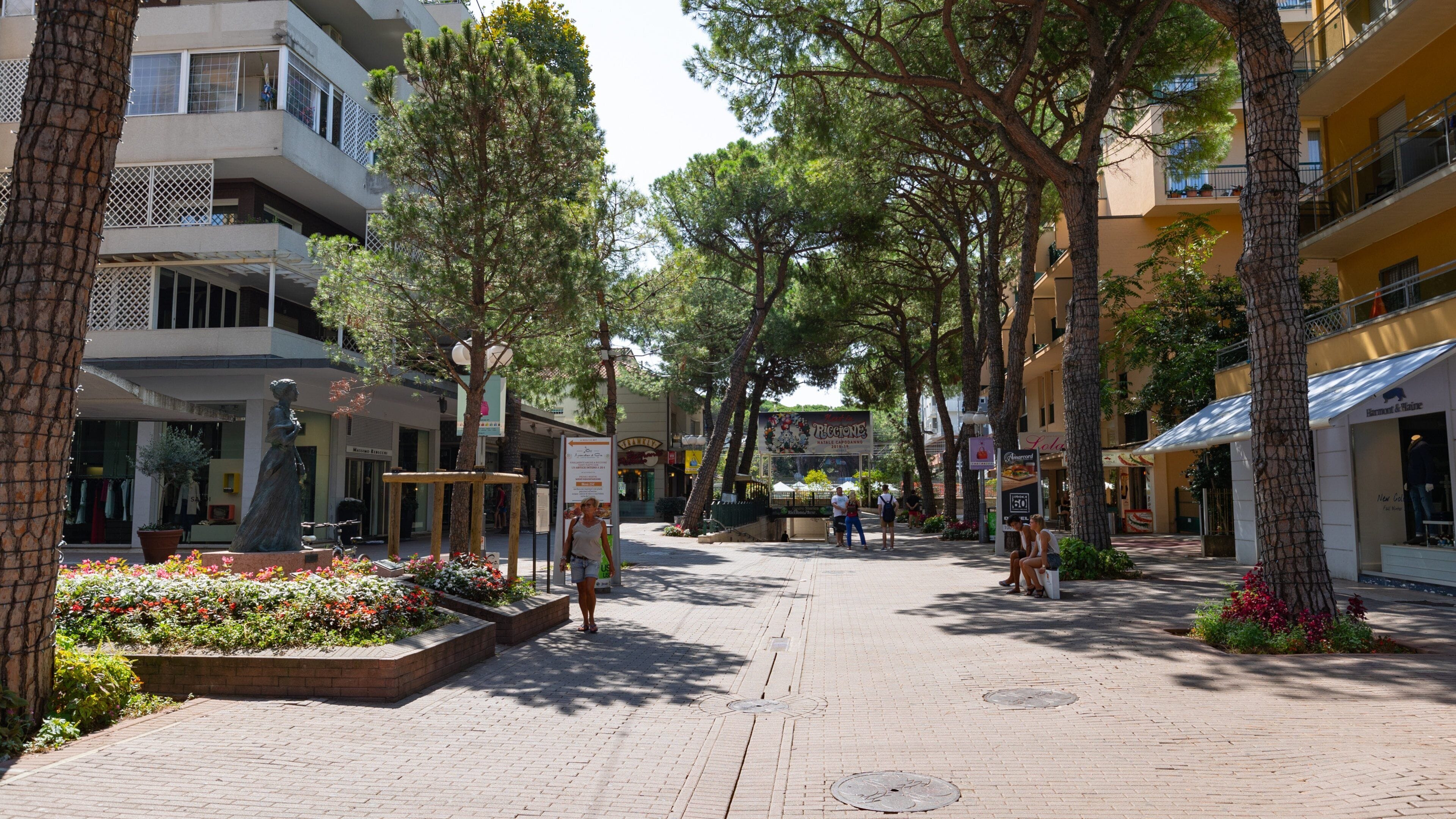 A tree-lined pedestrian street with buildings, shops, and outdoor seating areas.