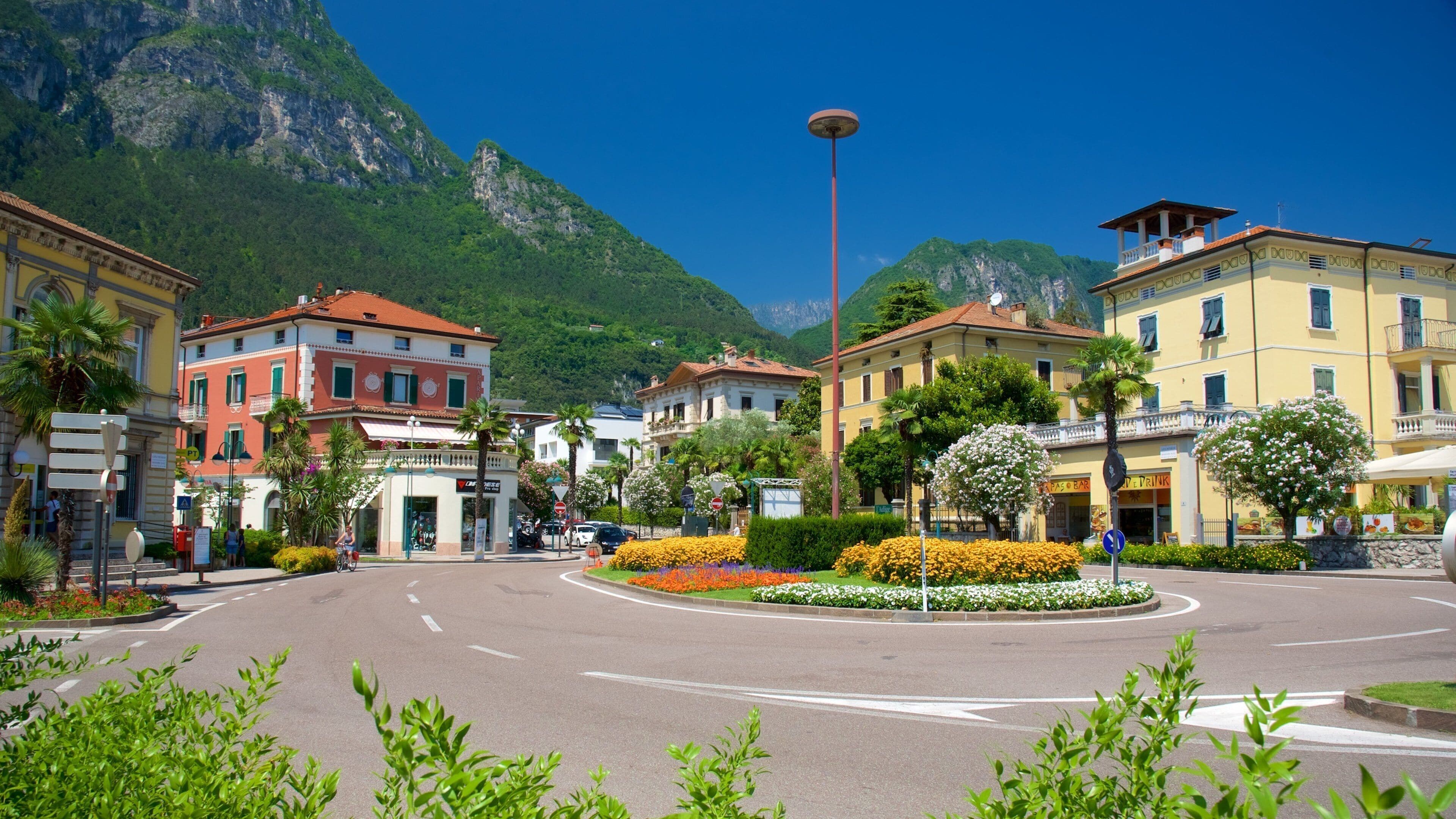 A town square with colorful buildings, a mountain backdrop, and a roundabout with flower beds.