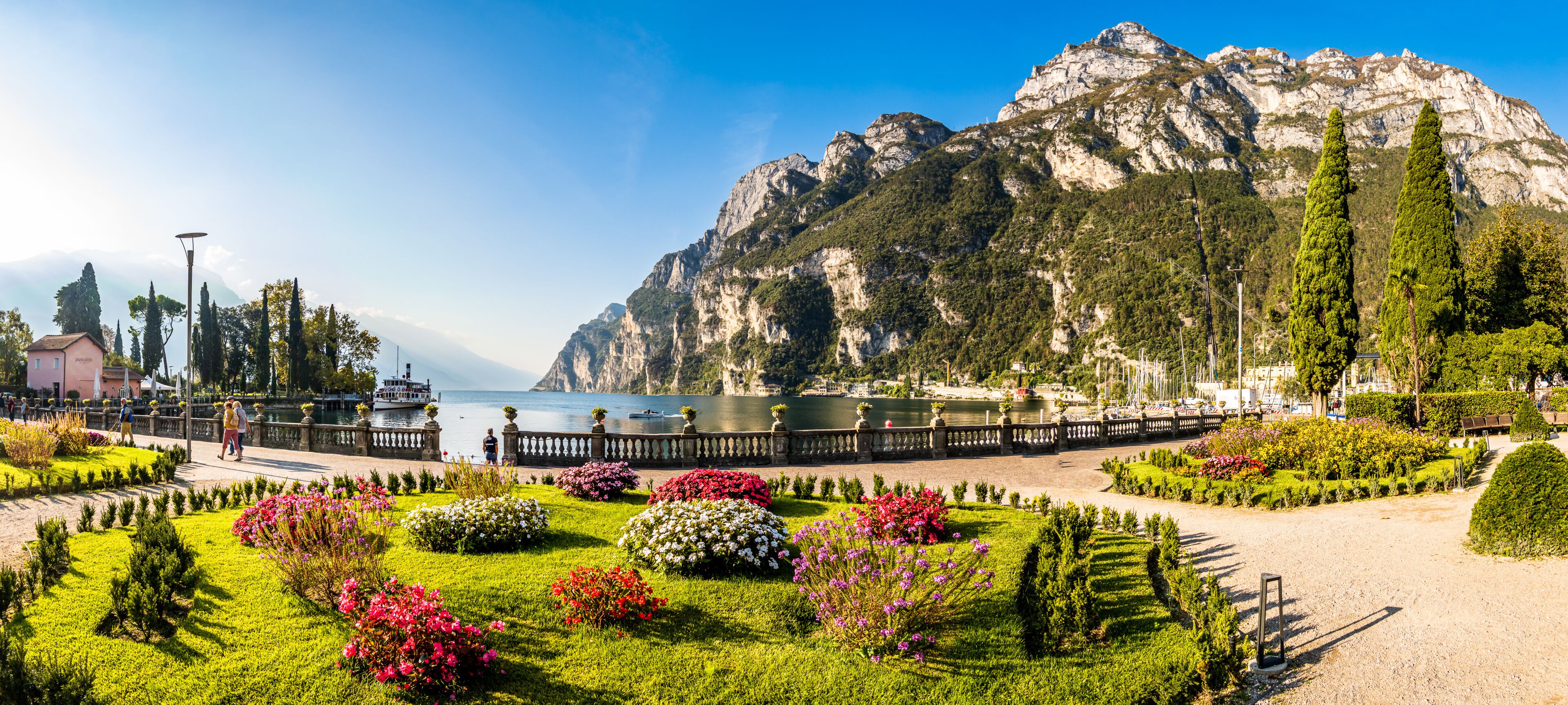 A landscaped garden with flower beds, a body of water, and a mountainous backdrop.
