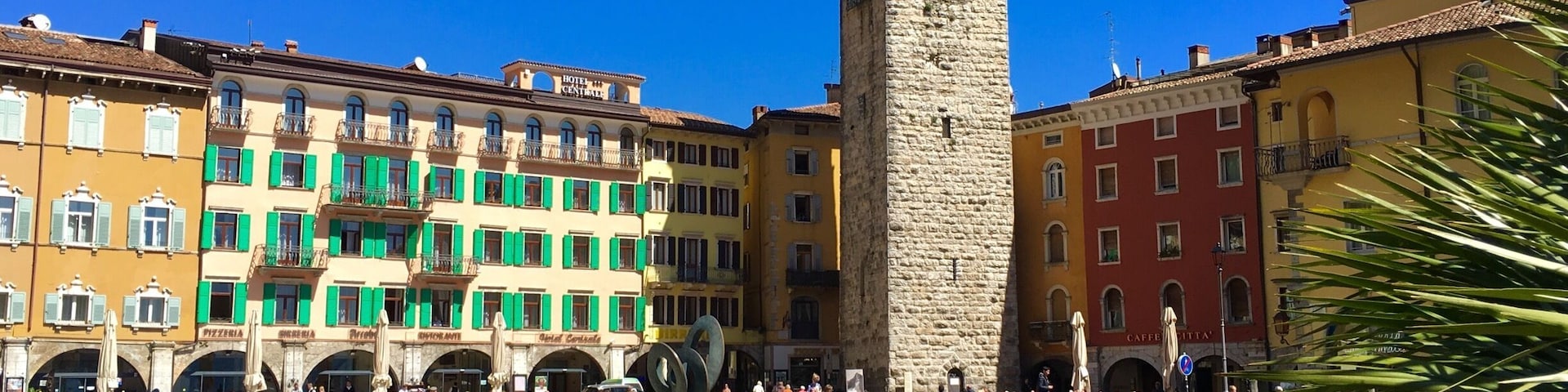 Uma praça histórica com uma torre imponente, edifícios coloridos e uma superfície aquática calma.