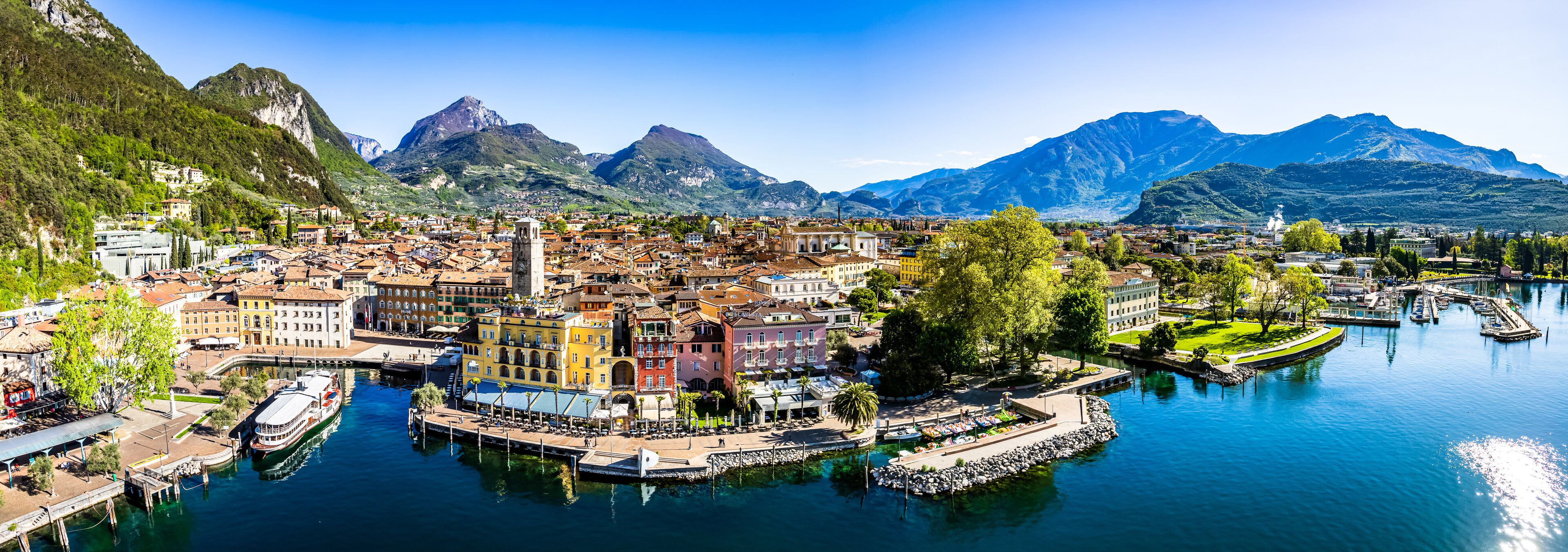 A coastal town with a marina, colorful buildings, and mountains in the background.