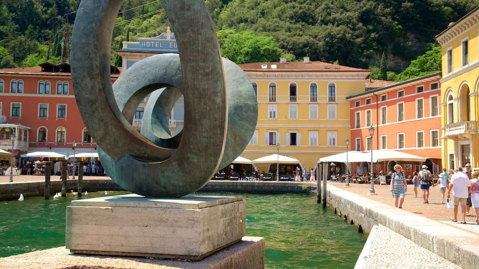 A sculpture in a public square with a water feature, surrounded by historic buildings and people.