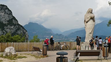 A stone statue, wooden benches, a bicycle, and a rocky mountain backdrop.