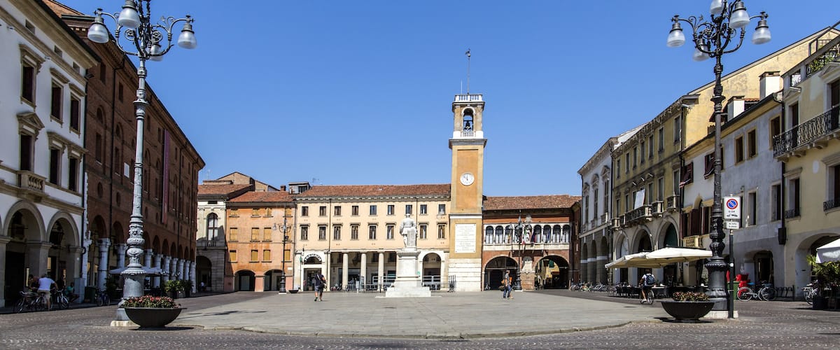 A cobblestone square with a central fountain, historic buildings, and a clock tower.