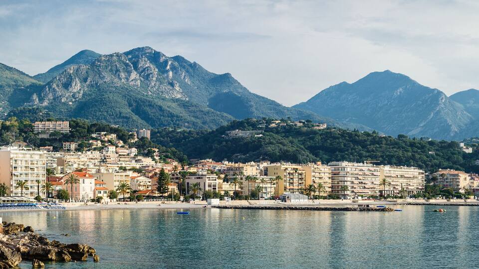 A coastal city with a mountain backdrop, featuring a beach, buildings, and rocky outcrops.