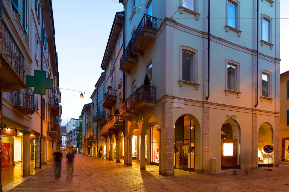 Uma rua de paralelepípedos ladeada por edifícios históricos, lojas e uma passarela para pedestres.