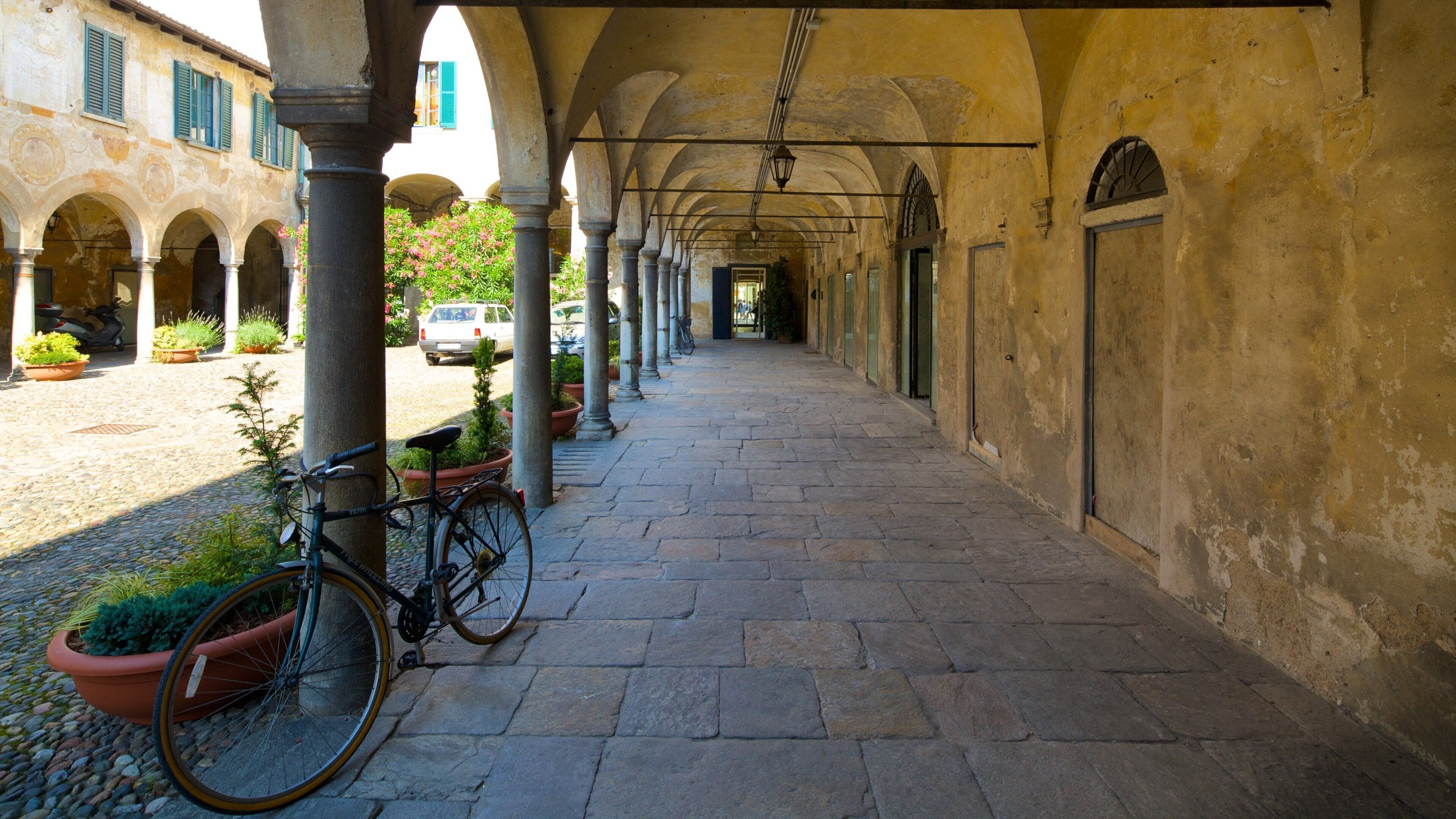 A stone-paved corridor with arches, potted plants, and a bicycle.