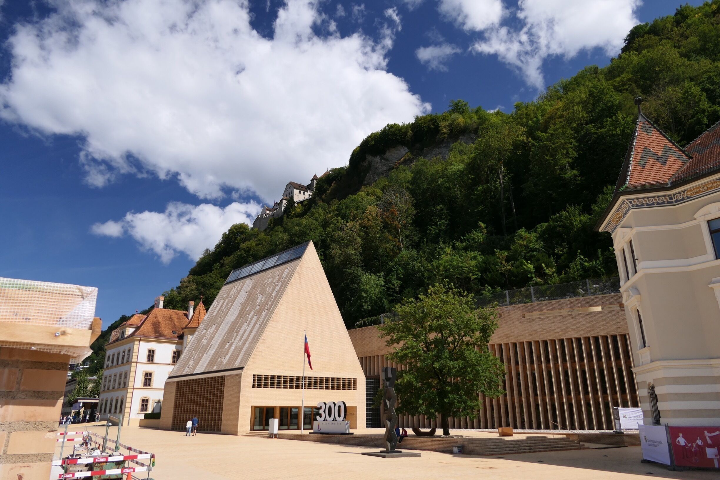 A historic building with a pyramid-shaped roof, surrounded by lush greenery and a clear blue sky.