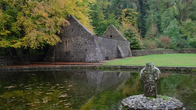A stone building with a pond in front, surrounded by trees and greenery.