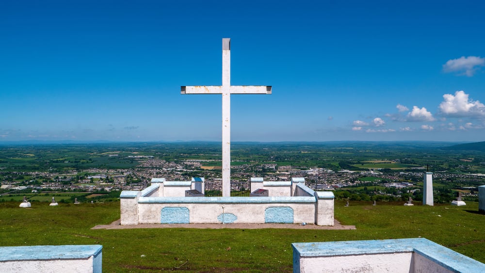 Ein großes weißes Kreuz auf einem Hügel, im Hintergrund eine Stadt.