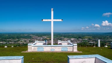 A large white cross on a hill with a town in the background.