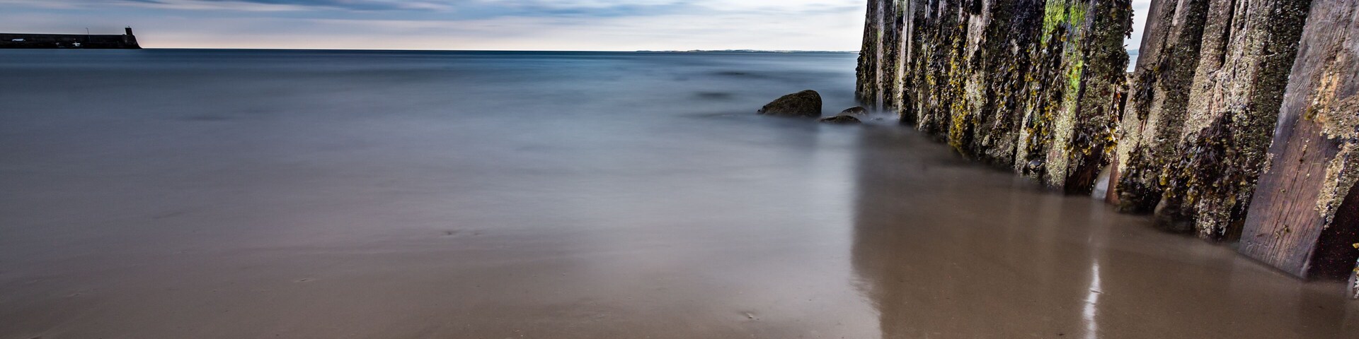 A beach with a long row of weathered wooden posts and a calm sea under a cloudy sky.