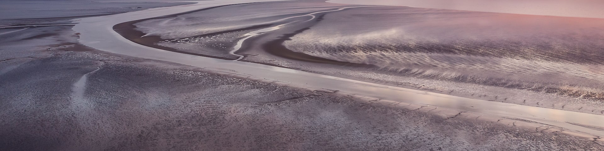 A winding road through a desert landscape with distant mountains and a sunset.