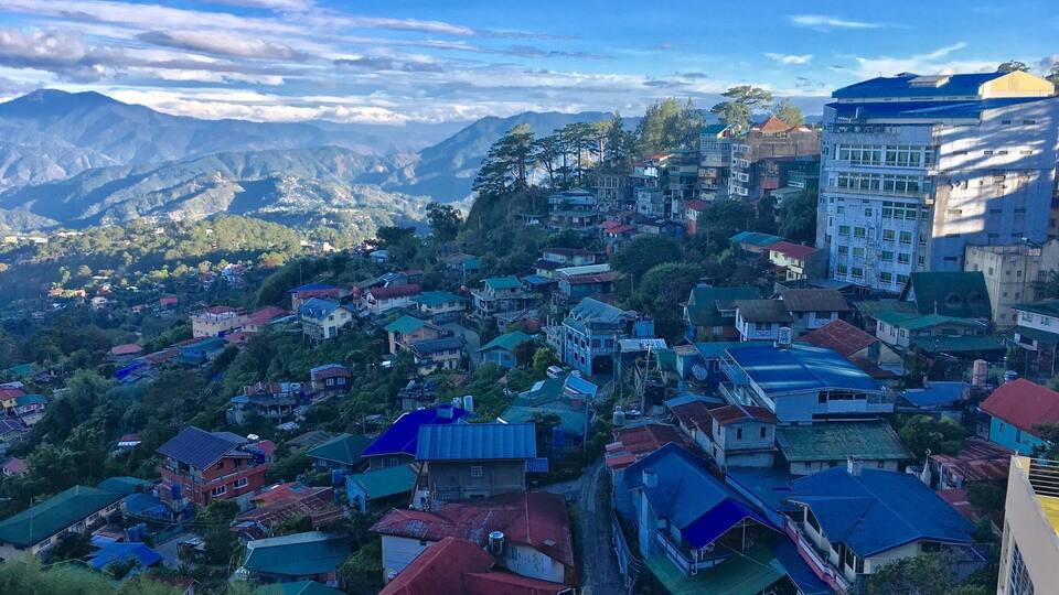 A mountainous town with colorful houses and buildings, surrounded by lush greenery and distant mountains.