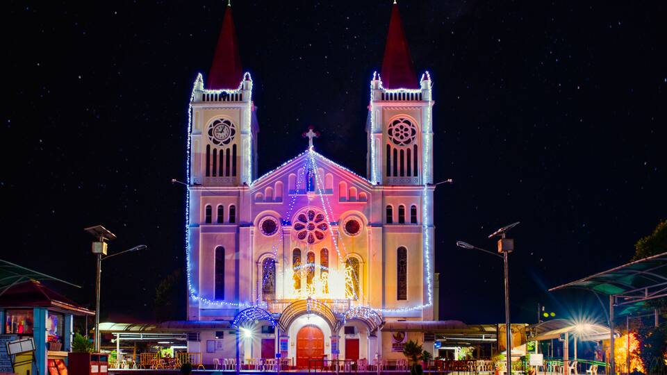 A brightly lit church with two towers and a large rose window.