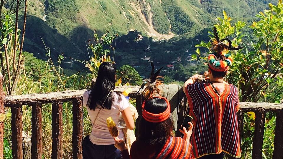 A group of people on a stone pathway overlooking a valley with green hills and a winding road.