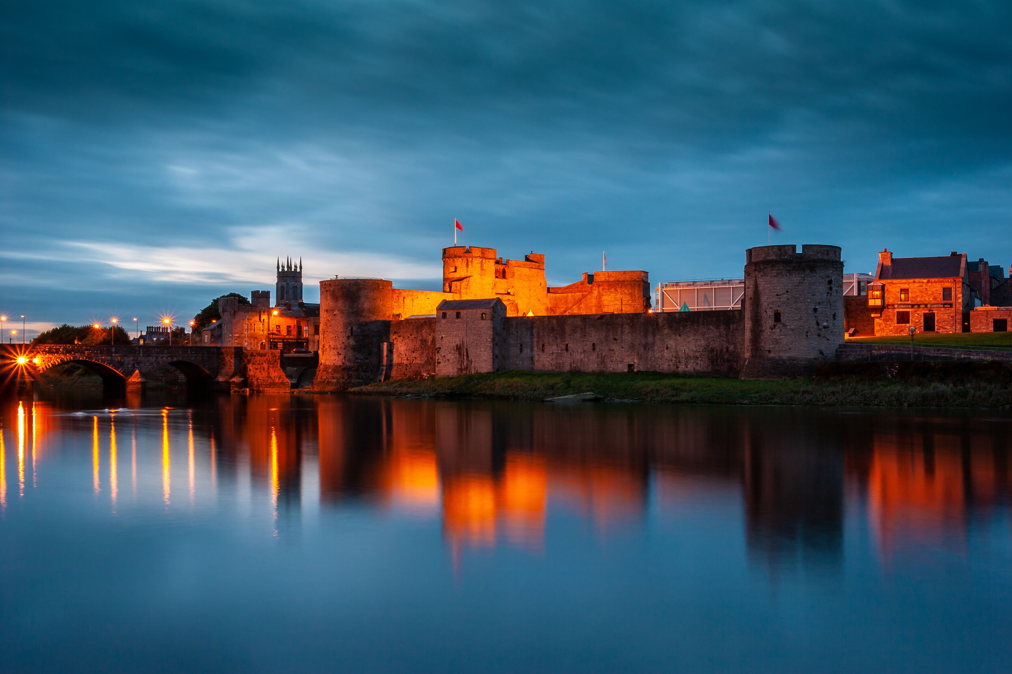 A historic castle with a moat, a bridge, and a river reflecting the structures.