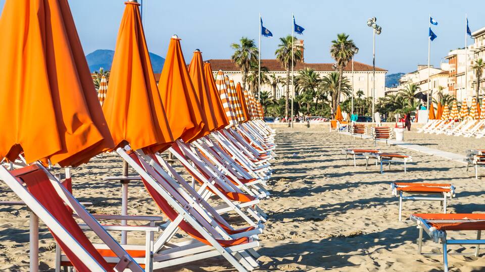 A beach with rows of orange umbrellas and white lounge chairs.