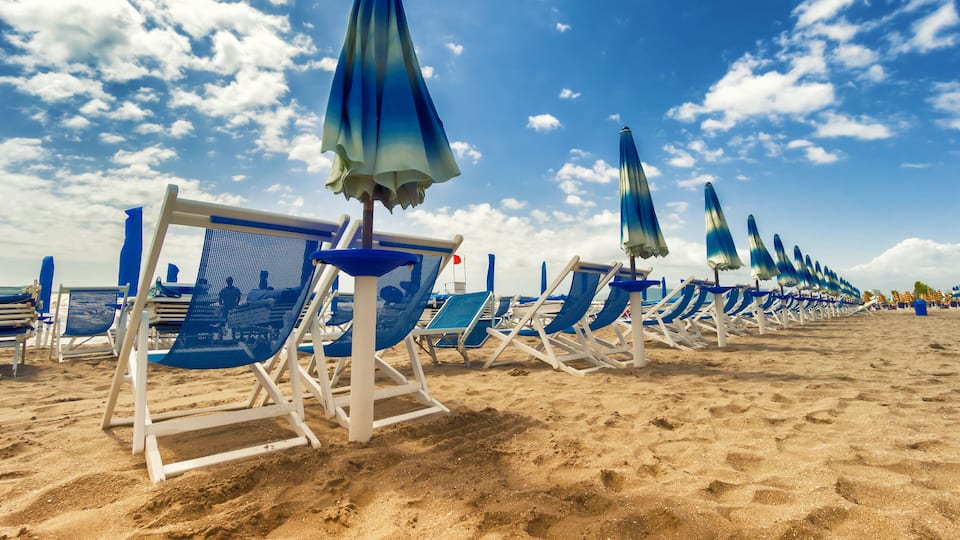 A beach with rows of blue lounge chairs and matching umbrellas under a clear sky.