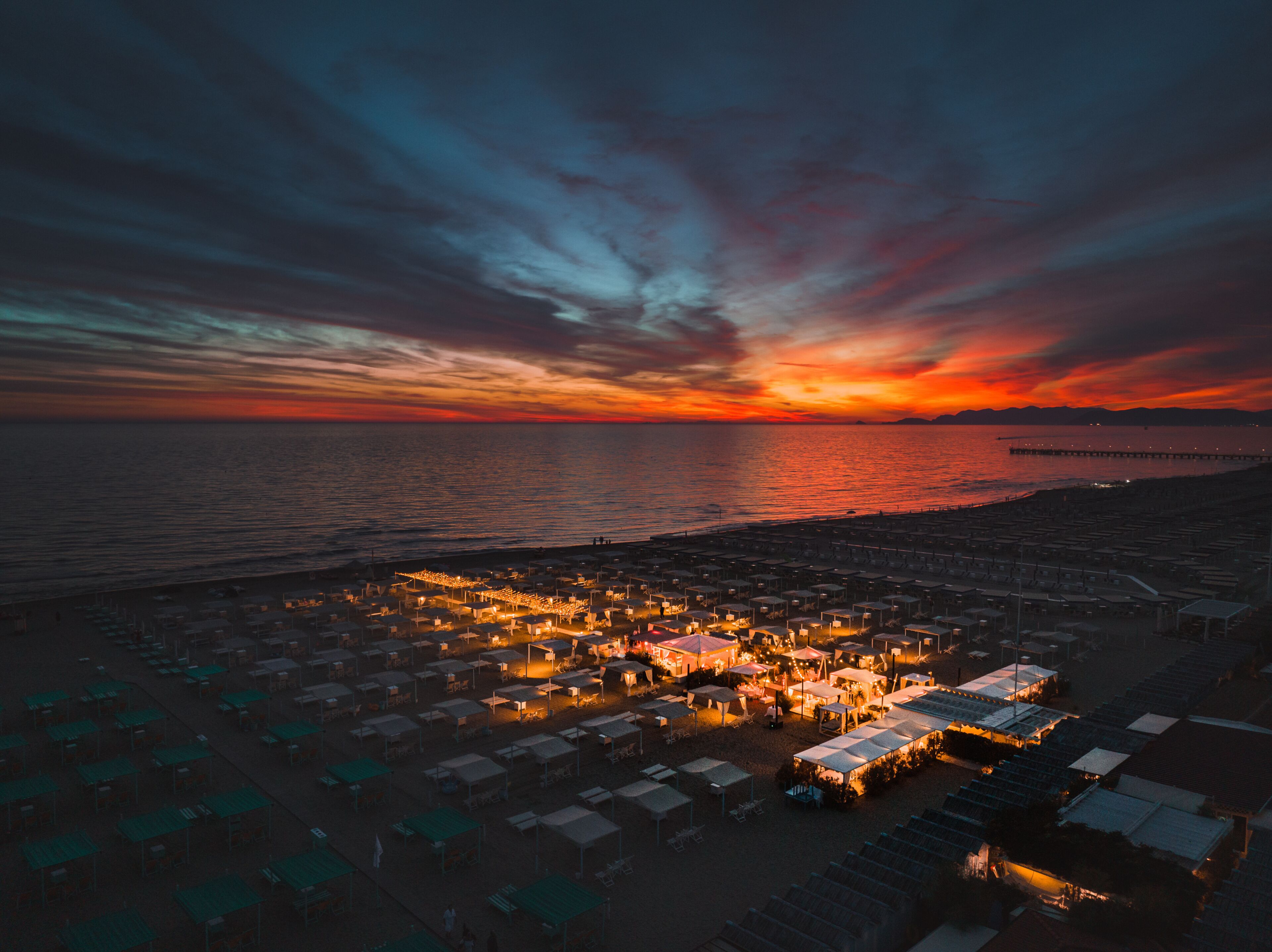 A coastal area with tents and a pier extending into the water during sunset.