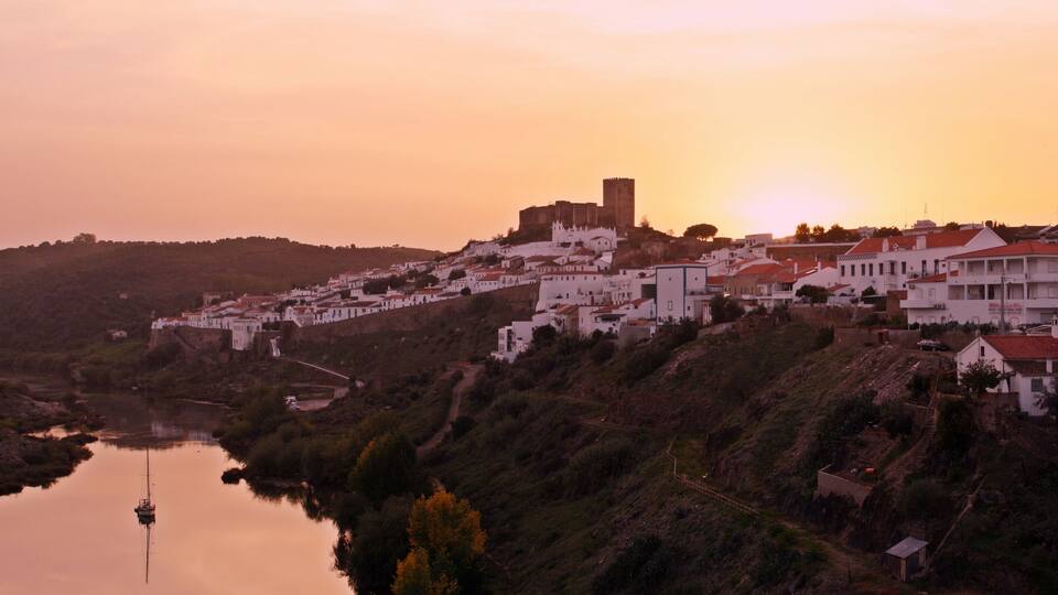 A coastal town with white buildings, a castle, and a river.