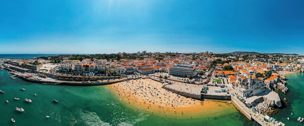 Eine Küstenstadt mit Sandstrand, einem Hafen voller Boote und historischen Gebäuden.