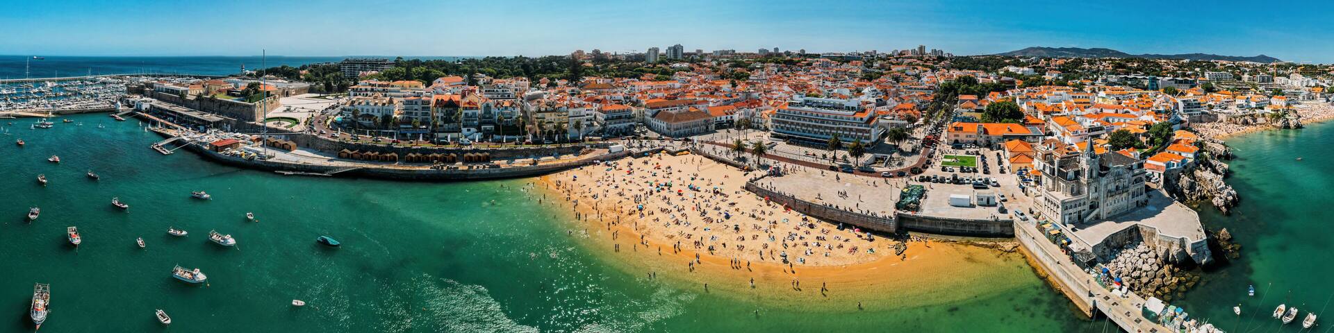 A coastal town with a sandy beach, a harbor with boats, and historic buildings.