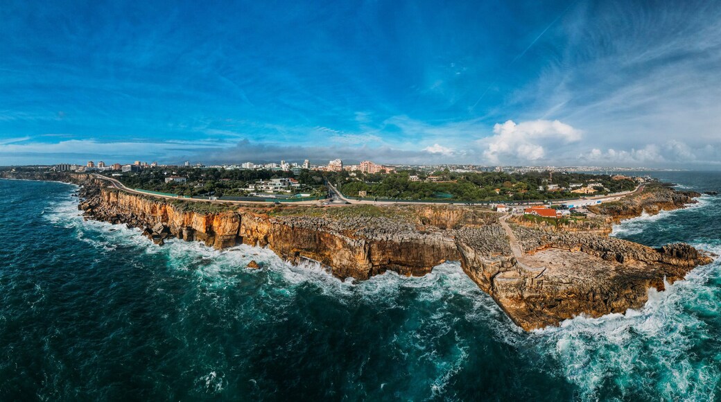 Paesaggio costiero con una prominente penisola rocciosa, un ponte che la collega alla terraferma e un cielo azzurro limpido.