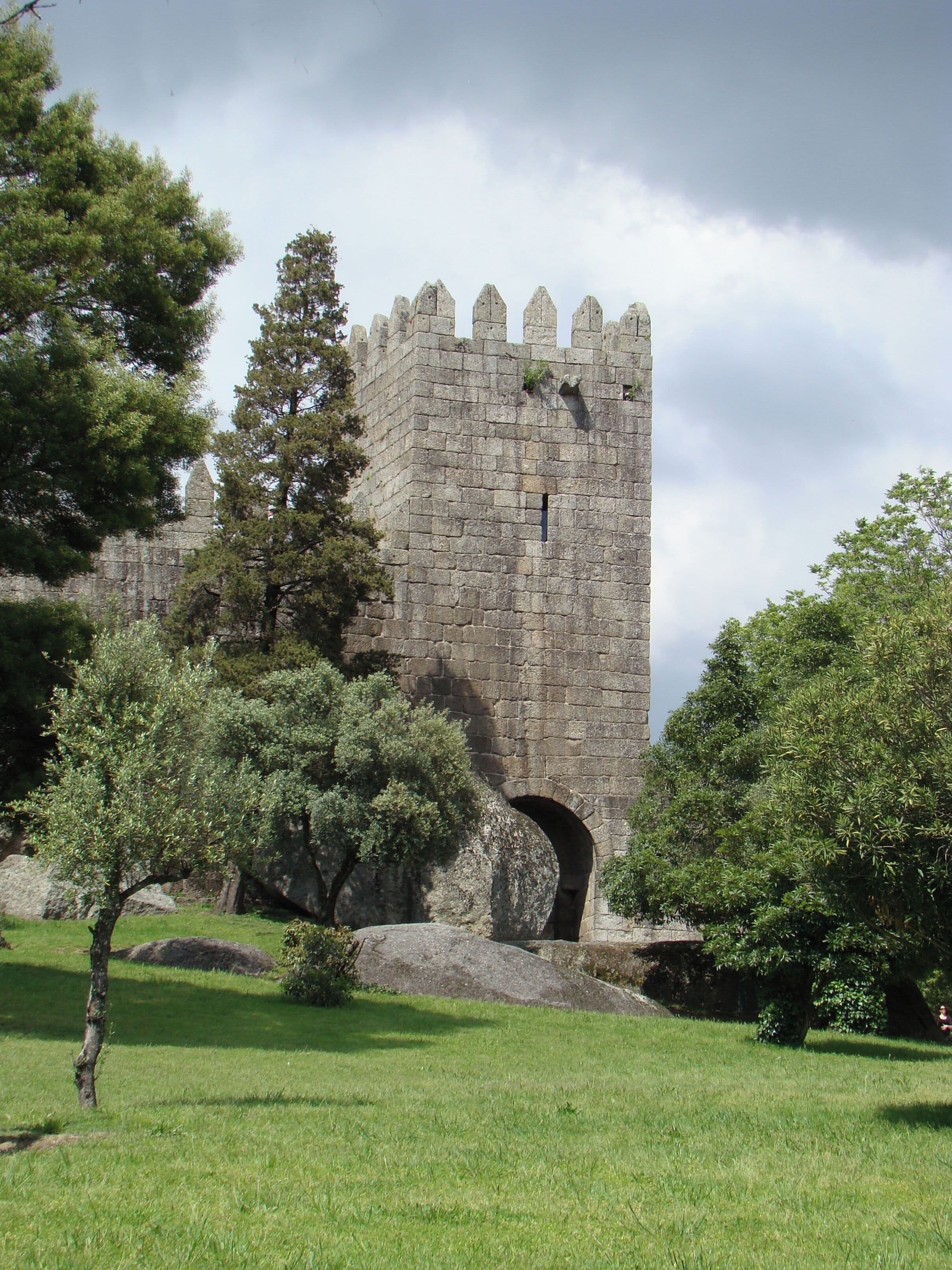 A historic stone castle with a tall tower and battlements, surrounded by lush greenery and trees.