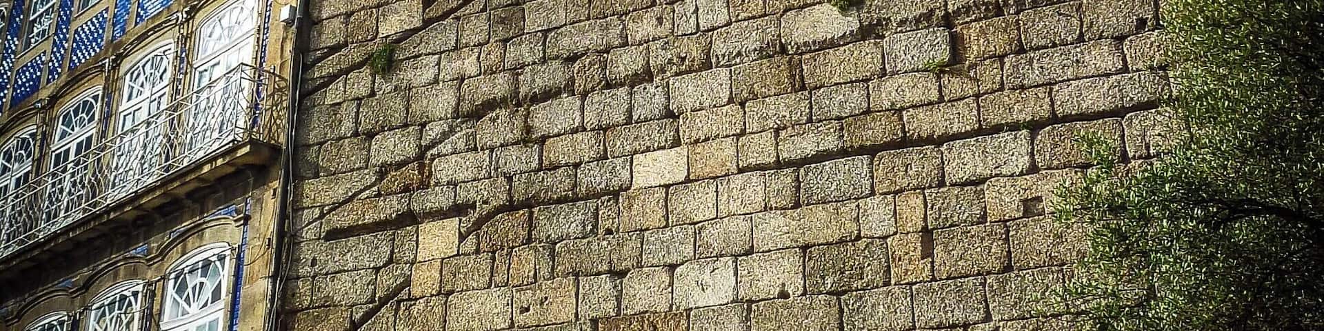 A stone wall with the inscription "AQUIT NASCEU PORTUGAL" and a building with blue and white patterned windows.