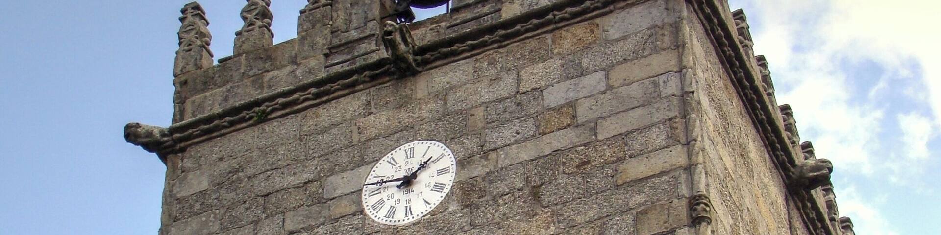 Una torre histórica con un reloj, ventanas arqueadas y un veleta.