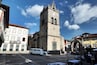 Une place historique, dominée par une tour imposante, bordée de rues pavées et entourée de bâtiments traditionnels.