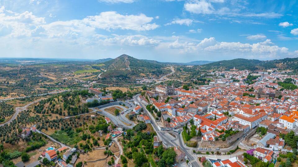 A panoramic view of a town with red-roofed buildings, a prominent hill, and a river.