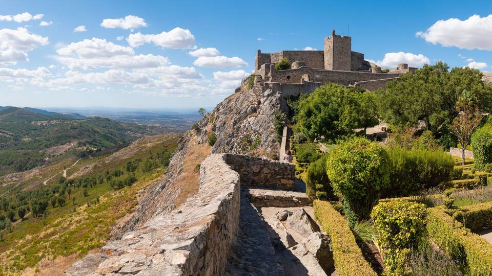 A historic stone castle on a hill with a view of the surrounding landscape.