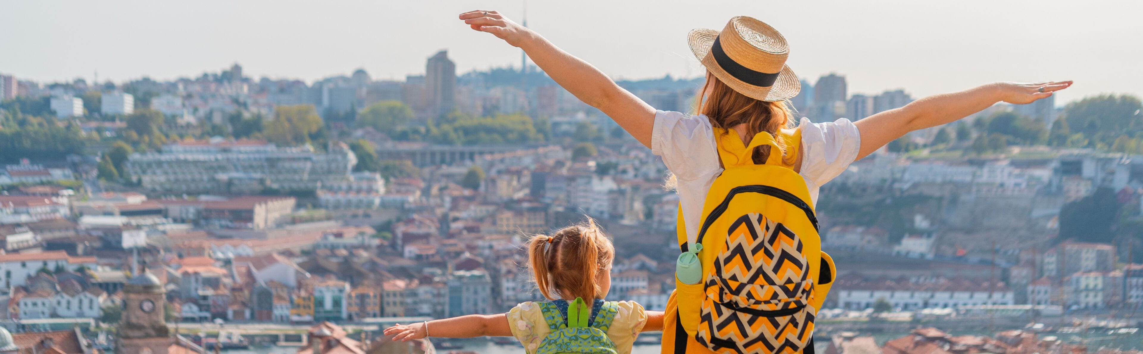View from behind of Young red-haired mother and little daughter raised thair hands up against the Porto city, Portugal