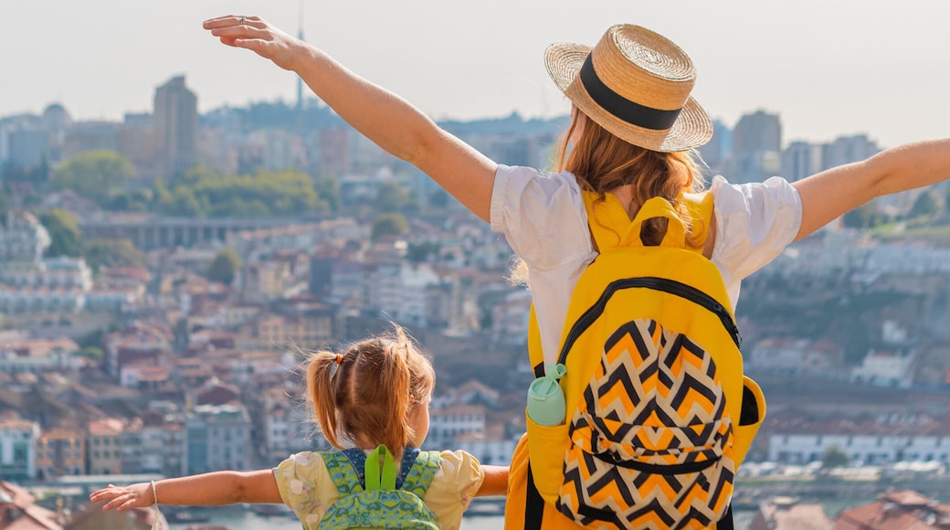 View from behind of Young red-haired mother and little daughter raised thair hands up against the Porto city, Portugal