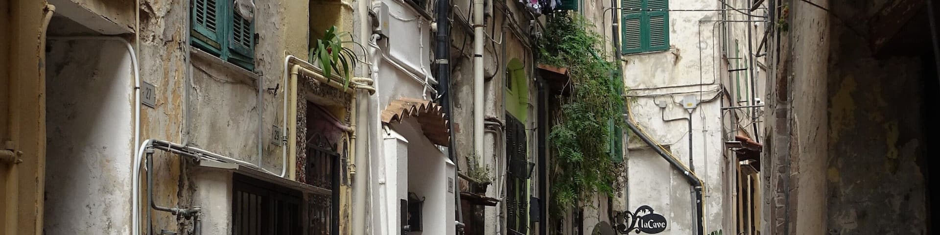 A narrow alleyway with old buildings, green shutters, and a sign for "LaCave".